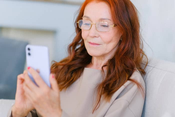 Vonzó vörös hajú nő mobiltelefonon ismerkedik társkereső alkalmazáson